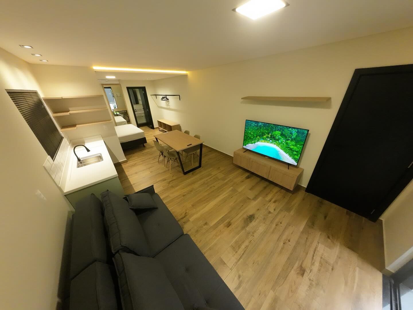 Ambiente integrado do Loft 1, com sala, cozinha, mesa e cama ao fundo
